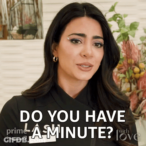 A Woman Says " Do You Have A Minute " In Front Of Flowers GIF