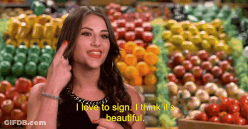 A Woman Says I Love To Sign I Think It 'S Beautiful In Front Of A Bunch Of Fruits And Vegetables GIF