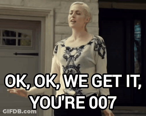 A Woman Says Ok Ok We Get It You 'Re 007 While Standing In Front Of A Garage Door GIF