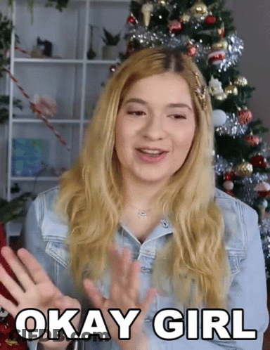 A Woman Says Okay Girl With A Christmas Tree In The Background GIF