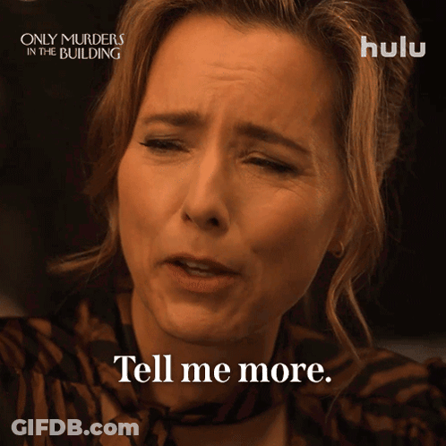 A Woman Says " Tell Me More " In Front Of A Poster For Only Murders In The Building GIF