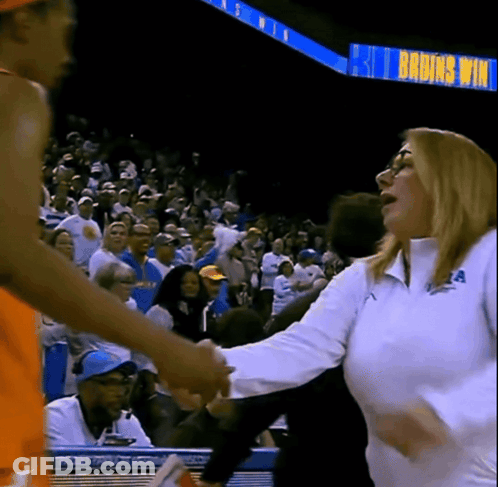 A Woman Shakes Hands With A Basketball Player In Front Of A Sign That Says Bruins Win GIF