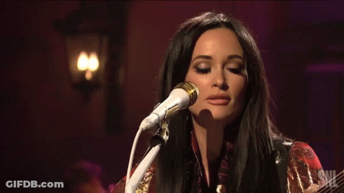 A Woman Singing Into A Microphone And Holding A Guitar GIF