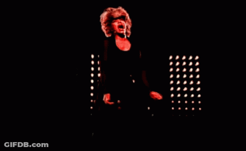 A Woman Singing Into A Microphone In A Dark Room With Red Lights GIF