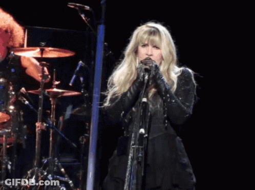 A Woman Singing Into A Microphone In Front Of A Drum Set GIF
