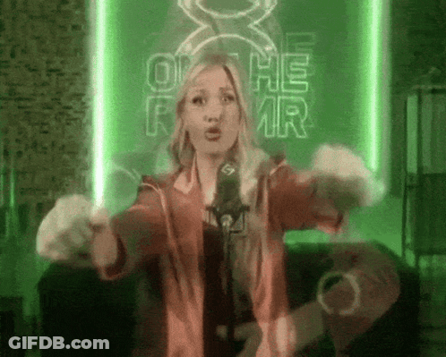 A Woman Singing Into A Microphone In Front Of A Green Sign That Says Oh He Mr. GIF