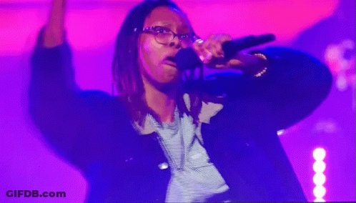 A Woman Singing Into A Microphone In Front Of A Purple Background GIF