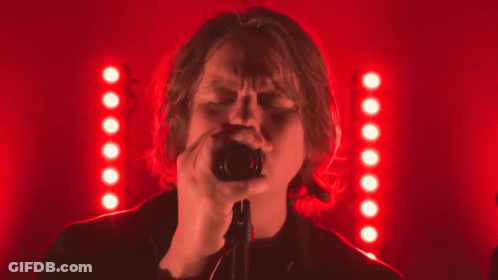 A Woman Singing Into A Microphone In Front Of A Red Background GIF