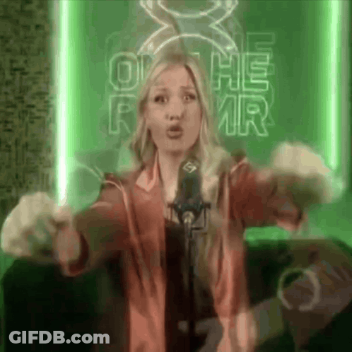 A Woman Singing Into A Microphone In Front Of A Sign That Says O He Rmr GIF