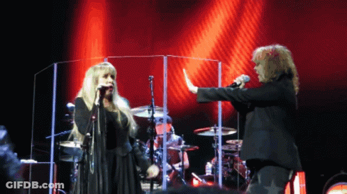 A Woman Singing Into A Microphone Next To A Man GIF