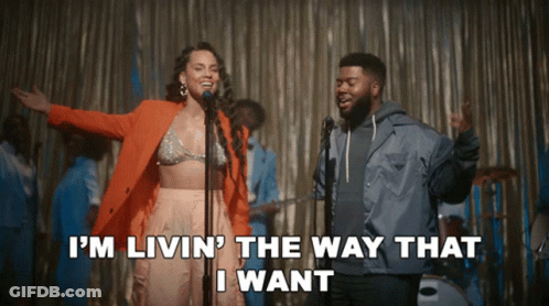 A Woman Singing Into A Microphone Next To A Man Who Says I 'M Livin GIF