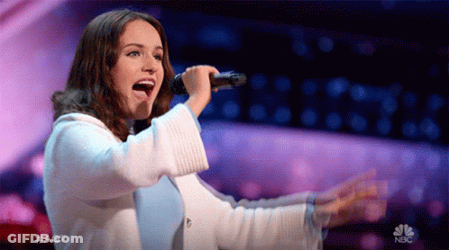 A Woman Singing Into A Microphone On A Stage With A Nbc Logo In The Background GIF