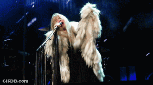 A Woman Singing Into A Microphone Wearing A White Fur Coat GIF