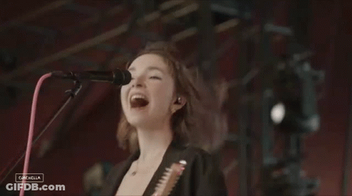 A Woman Singing Into A Microphone While Holding A Guitar In Front Of A Coachella Logo GIF