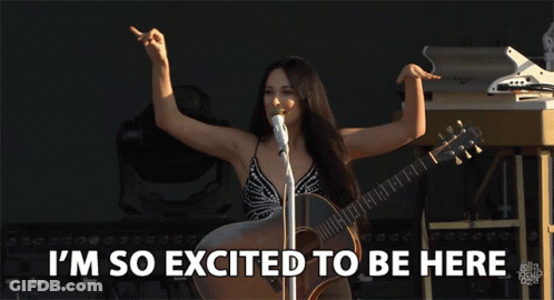 A Woman Singing Into A Microphone While Holding A Guitar With The Words I 'M So Excited To Be Here Below Her GIF
