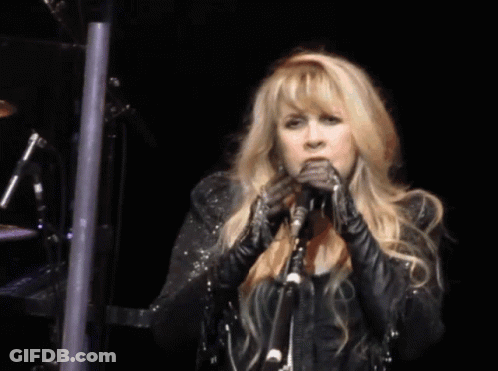 A Woman Singing Into A Microphone While Wearing A Black Jacket GIF