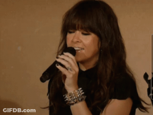 A Woman Singing Into A Microphone While Wearing A Bracelet With Spikes GIF