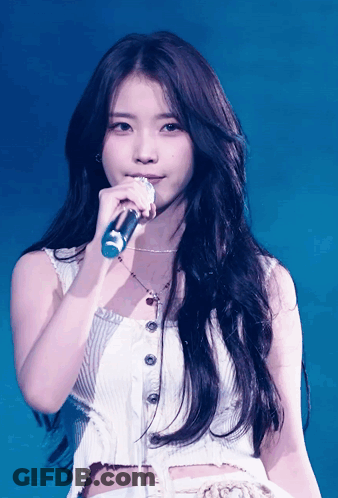 A Woman Singing Into A Microphone While Wearing A White Tank Top GIF