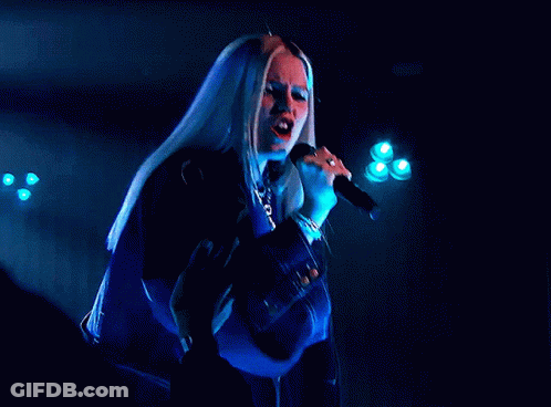 A Woman Singing Into A Microphone With A Blue Background GIF