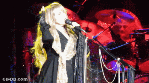 A Woman Singing Into A Microphone With A Drummer Behind Her GIF