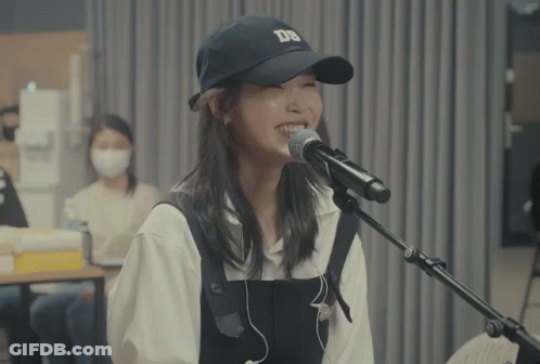 A Woman Singing Into A Microphone With A Ds Hat On GIF