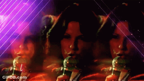 A Woman Singing Into A Microphone With A Purple Background Behind Her GIF