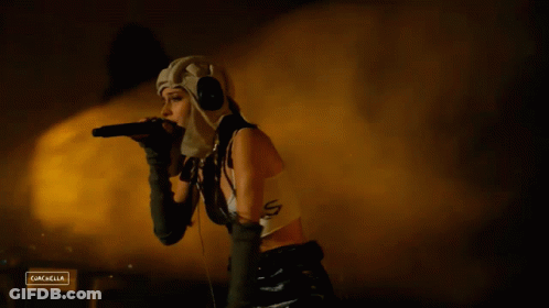 A Woman Singing Into A Microphone With A Sign That Says Campella On The Bottom GIF
