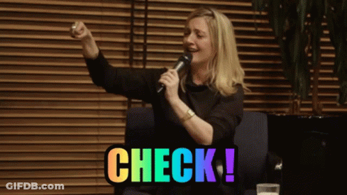 A Woman Singing Into A Microphone With Check Written In Rainbow Colors Behind Her GIF