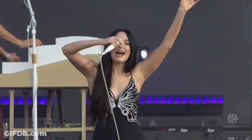 A Woman Singing Into A Microphone With Her Arms Outstretched GIF