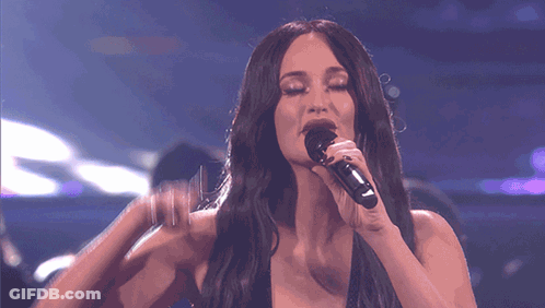 A Woman Singing Into A Microphone With Her Hand On Her Face GIF