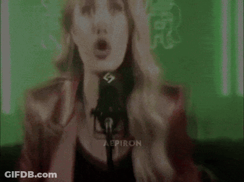 A Woman Singing Into A Microphone With The Letters Aep On Her Chest GIF