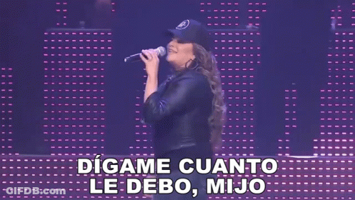 A Woman Singing Into A Microphone With The Words " Digame Cuanto Le Debo Mijo " Behind Her GIF