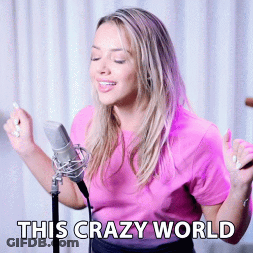 A Woman Singing Into A Microphone With The Words " This Crazy World " Below Her GIF