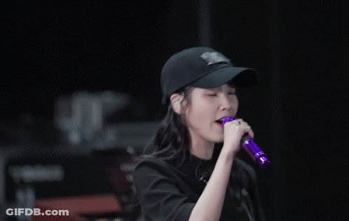 A Woman Singing Into A Purple Microphone Wearing A Baseball Cap GIF