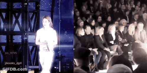A Woman Singing On Stage Next To A Group Of People GIF