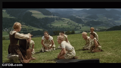 A Woman Singing To A Group Of Children On A Hill GIF