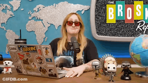 A Woman Sits At A Desk With A Laptop And A Microphone In Front Of A Sign That Says The Broski Reg GIF
