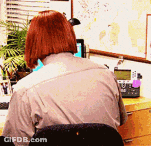 A Woman Sits At A Desk With A Telephone And A Map On The Wall Behind Her GIF