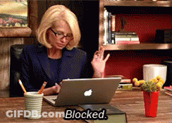 A Woman Sits At A Desk With An Apple Laptop And The Word Blocked On The Table GIF