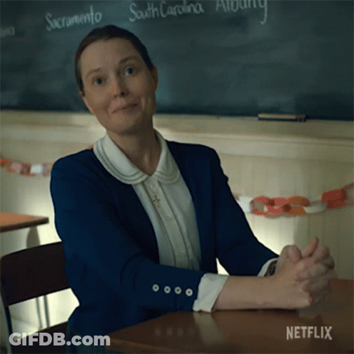 A Woman Sits At A Desk With Her Hands Folded In Front Of A Blackboard That Says South Carolina On It GIF