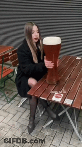 A Woman Sits At A Table Holding A Giant Beer Glass GIF