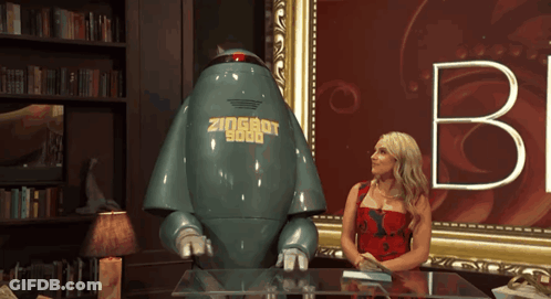 A Woman Sits At A Table Next To A Robot That Says Zioshot 9000 On It GIF