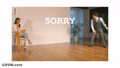 Woman Sitting At Table While Man Dances In Front Of Sorry Wall GIF