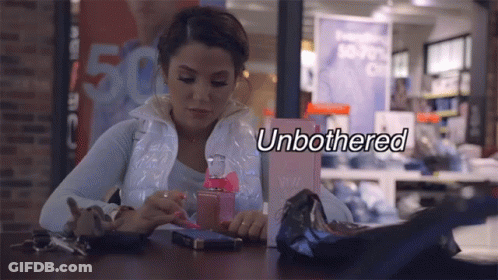 A Woman Sits At A Table With A Bottle Of Perfume And The Word Unbothered Written Above Her GIF