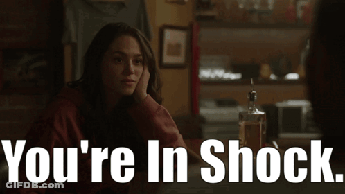 A Woman Sits At A Table With A Bottle Of Whiskey And The Words " You 'Re In Shock " Above Her GIF