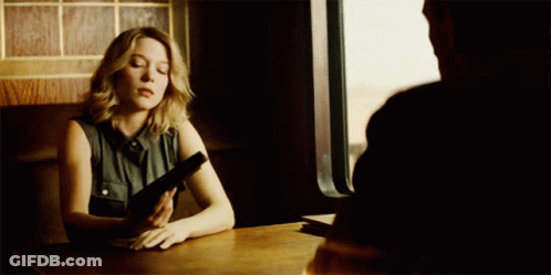 A Woman Sits At A Table With A Gun In Her Hand GIF