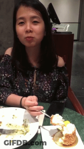 A Woman Sits At A Table With A Plate Of Food And A Piece Of Cake GIF
