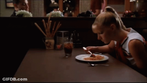 A Woman Sits At A Table With A Plate Of Food On It GIF