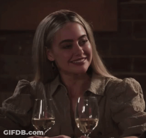 A Woman Sits At A Table With Two Glasses Of Wine In Front Of Her GIF