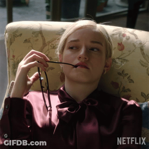 A Woman Sits In A Chair Holding A Pair Of Glasses In Her Mouth GIF